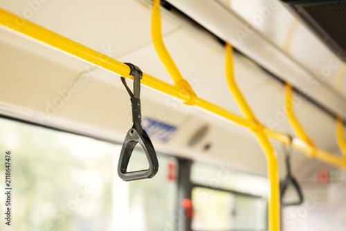 Black grab handle strap hanging on yellow handrail in public transport interior. Safety equipment for standing passengers in city bus, train, or tram.