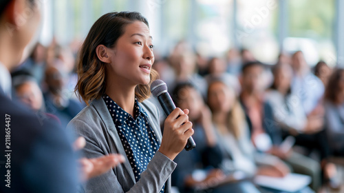 Hosting a bright medical conference, a professional moderator interviews a female pharmaceutical executive before a diverse audience, generic biotechnology graphics, no logos, healthcare,