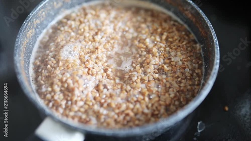 Buckwheat groats boiling and bubbling in a small saucepan on a kitchen stove during home cooking
