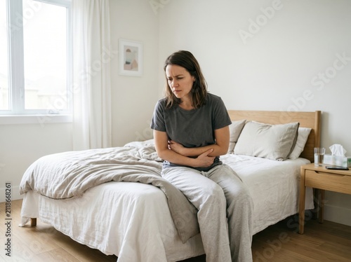 Young woman suffering from abdominal pain sitting on bed at home.