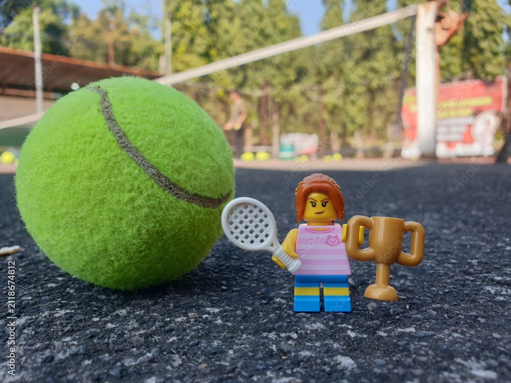 Fototapeta premium Indonesia - August 31, 2024 : Mini toy of action figure at tenniscourt with blurred background. Sport photography concept design. Miniature Young girl with trophy and tennis racket. Winning athlete.