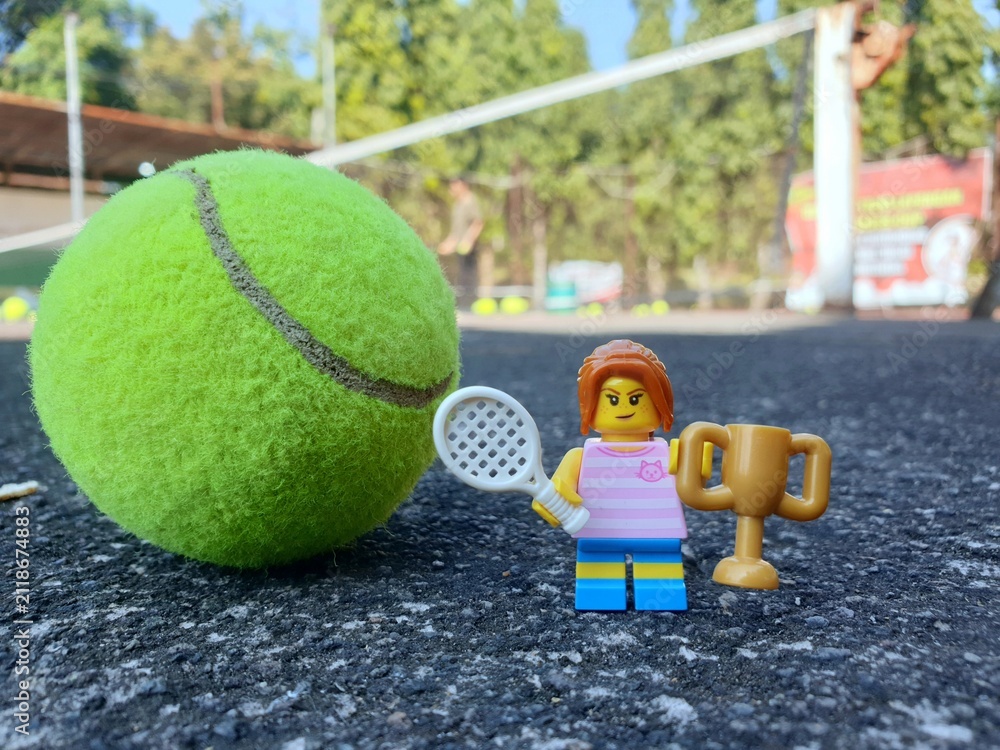 Fototapeta premium Indonesia - August 31, 2024 : Mini toy of action figure at tenniscourt with blurred background. Sport photography concept design. Miniature Young girl with trophy and tennis racket. Winning athlete.