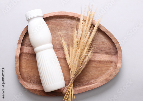 White plastic bottle of cereal yogurt and wheat ears in wooden tray on a gray background. Healthy eating concept.