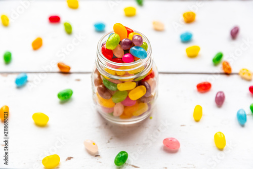 Glass of colourful sweet jellybeans on white wood