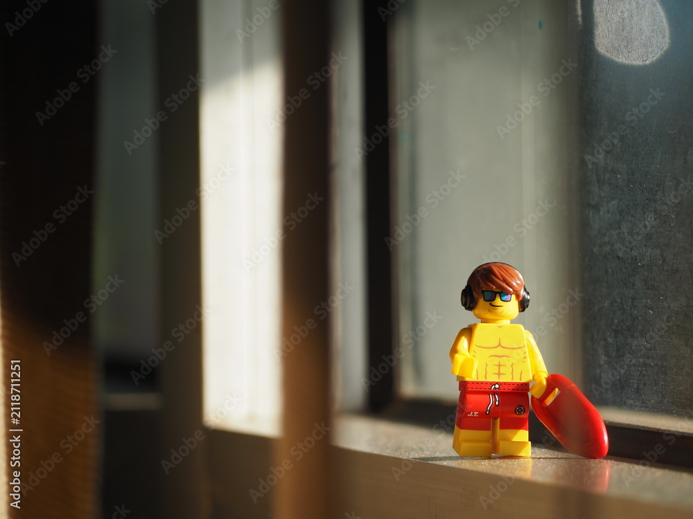 Fototapeta premium Indonesia - September 12, 2025 : Mini toy of action figure at table with blurred background. Miniature photography concept design. Minifigure of young man character with surf board at sunset time.