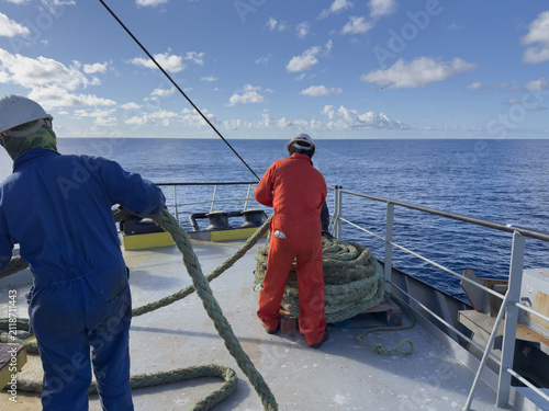 Foto Seamen preparing ropes on ship deck under bright blue sky.