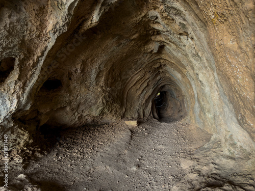 Foto Dark subterranean limestone cave tunnel with rough textured rock formations, lea