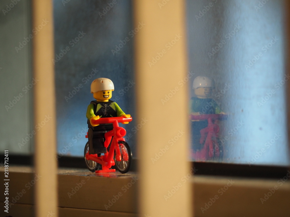 Fototapeta premium Indonesia - September 19, 2019 : Mini toy of action figure at outdoor with blurred background. Miniature photography concept design. Minifigure of young man character riding bicycle at road.
