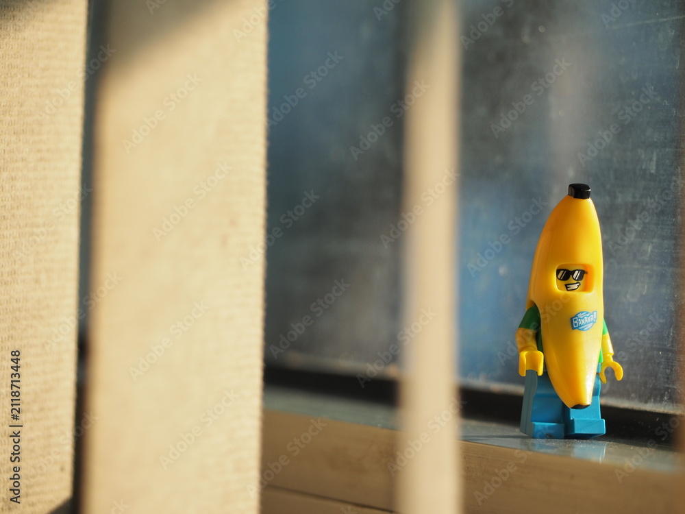 Fototapeta premium Indonesia - September 12, 2025 : Mini toy of action figure at table with blurred background. Miniature photography concept design. Minifigure of banana guy character at office window with sunset light