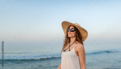 Картината върху платно Smiling young woman wearing sun hat and sunglasses enjoying a peaceful beach vac