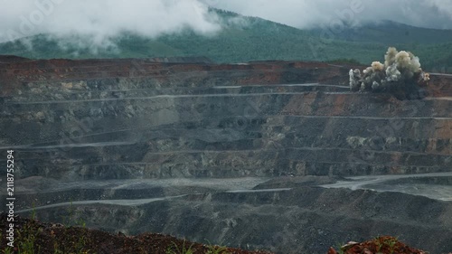 Slow motion explosive blast in open pit mine quarry with smoke and dust on mountainside.