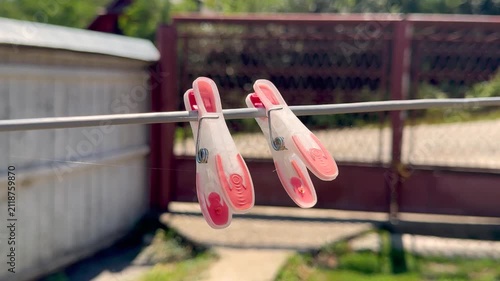 Two pink translucent plastic clothespins hanging on outdoor clothesline with thin spider web in sunny countryside backyard