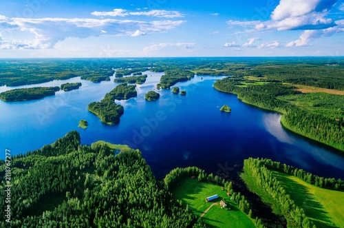 Aerial view of lush green forests surrounding tranquil blue lakes under bright blue sky in Finland