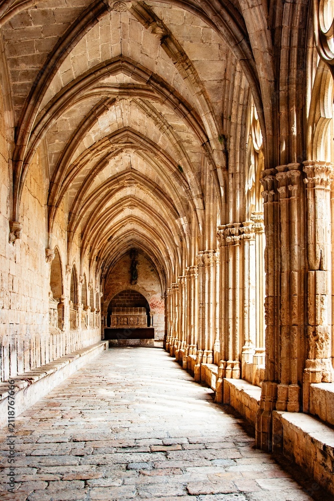 Fototapeta premium Stone arches and columns in a medieval cloister with sunlight illuminating the hallway