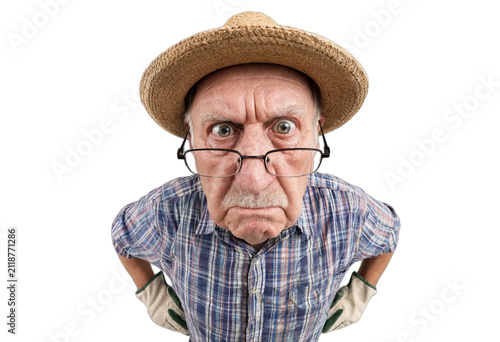 Elderly man frowning and staring directly at camera while wearing a straw hat, glasses and gardening gloves. High contrast portrait on a white background with copy space.