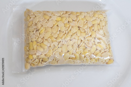 Peeled split soybeans packed tightly in a clear plastic zipper pouch, presented on a plain white surface. Highlighting raw plant based ingredients, prep work