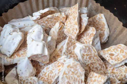 Sliced raw organic tempeh block on a clean white plate. Close up view showing the rich texture of fermented soybeans bound together by white mycelium. A healthy, plant-based vegan protein