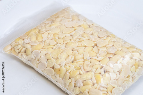 Peeled split soybeans packed tightly in a clear plastic zipper pouch, presented on a plain white surface. Highlighting raw plant based ingredients, prep work