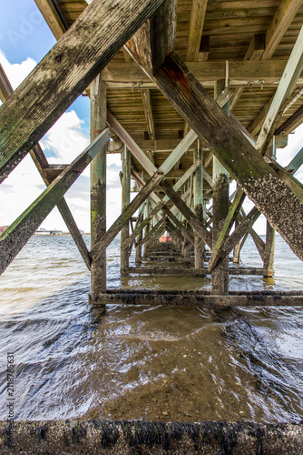 The underside of a pier or jetty on the coastline, wooden beams and pillars on the seabed.