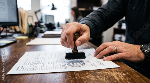 Closeup of a person stamping an official document on a wooden office desk