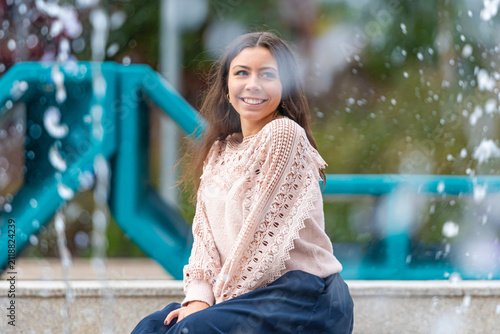 Young Woman Relaxing by a Fountain in an Urban Park During a Sunny Afternoon