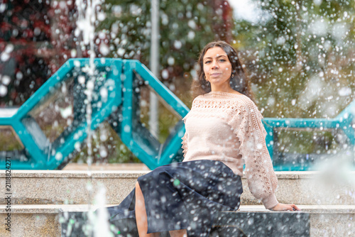 Young Woman Enjoys Relaxing Moment by Fountain in City Park on a Sunny Day