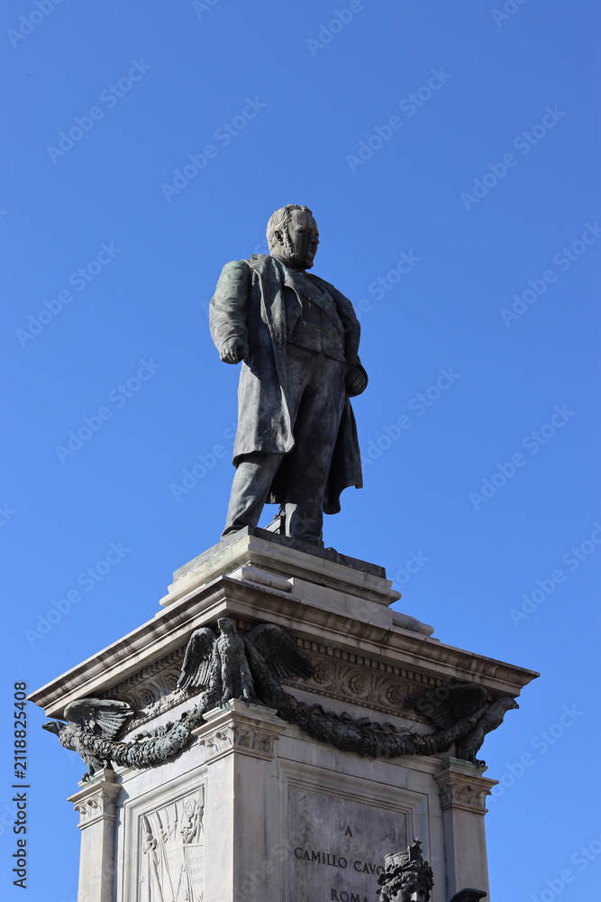 Fototapeta premium A bronze statue of Camillo Cavour stands atop an ornate stone pedestal against a clear blue sky.