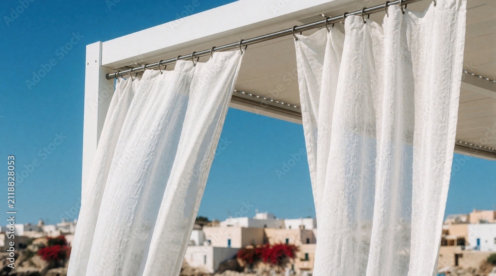 Obraz premium White linen curtains hang from a modern pergola with a bright blue sky and distant white village. Outdoor shelter offers privacy and shade by the sea.