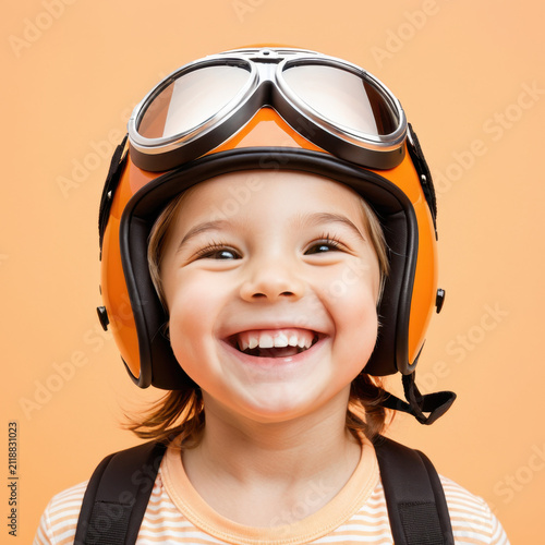 Cute little girl wearing retro aviator goggles and helmet smiling on beige background.