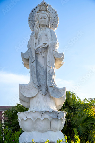 Bild auf Leinwand White marble Guanyin bodhisattva statue with halo standing on a lotus base against blue sky