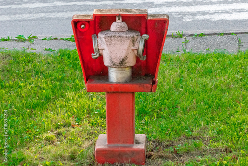 Red outdoor fire hydrant on green grass beside paved road