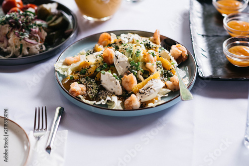 Fresh shrimp salad with soft cheese, avocado, orange slices, sesame seeds and herbs served in a modern restaurant. Healthy gourmet seafood meal on a stylish table, perfect for lunch, dinner and fine