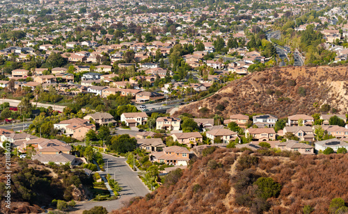 Cuadro en lienzo Elevated view of solar-equipped suburban homes beneath a dry chaparral ridge with hazy mountains beyond in Corona, California