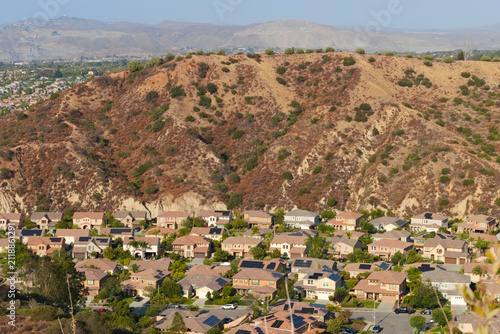Cuadro en lienzo Elevated view of solar-equipped suburban homes beneath a dry chaparral ridge with hazy mountains beyond in Corona, California