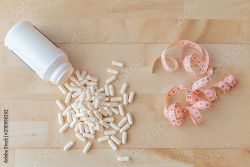 White Dietary Supplement Capsules with Measuring Tape on Wooden Background, Weight Loss and Fitness Concept