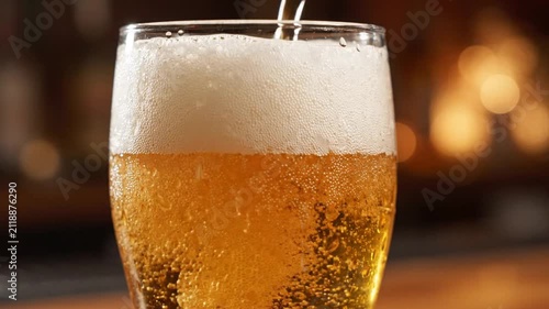 Cold beer pouring into glass, refreshing foam, bubbles, close-up, bar background, slow motion