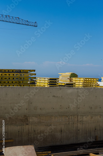 фотографія Construction site with stacked yellow formwork panels behind concrete wall and c