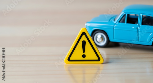 Yellow warning sign with exclamation mark and blue toy car on wooden surface