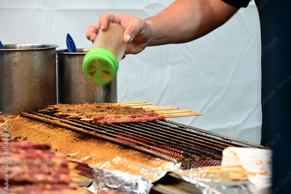 Fototapeta premium Charcoal grilled meat skewers are seasoned with powder by hand at a food stall in Banqiao Christmasland Market, Banqiao District, New Taipei City, Taiwan.