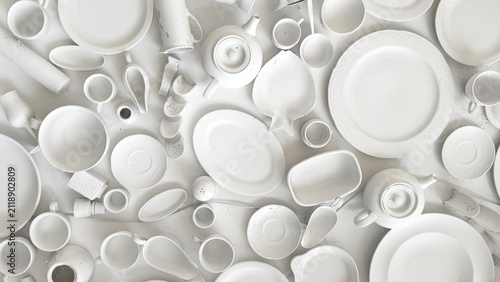 Variety of white ceramic plates and bowls with different shapes hanging on a white wall creating a decorative display