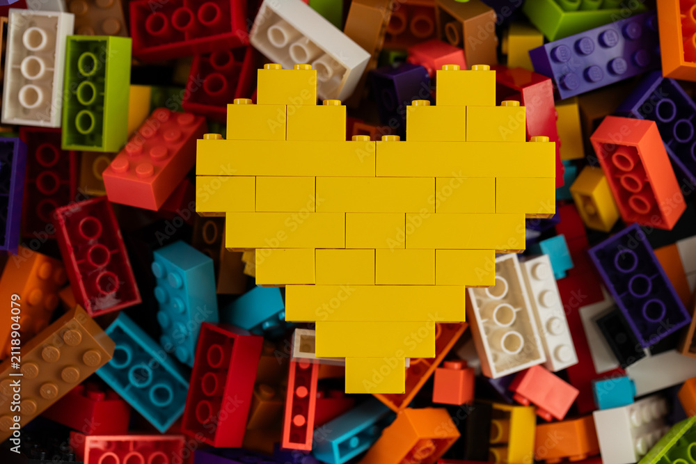 Fototapeta premium Yellow heart built from Lego bricks on colorful background of Lego pieces