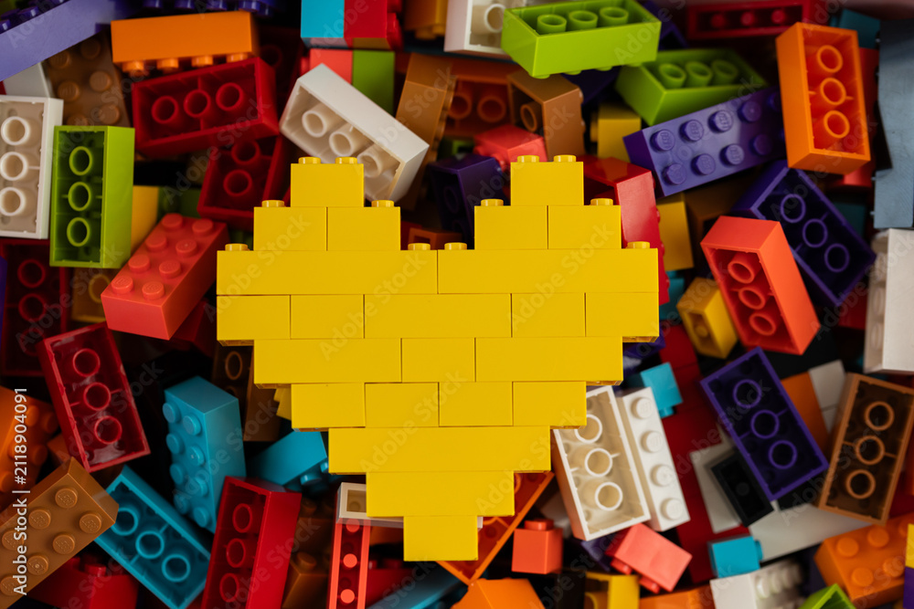 Fototapeta premium Yellow heart built from Lego bricks on colorful background of Lego pieces