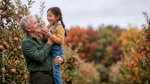 grandfather holds his granddaughter in his arms during a walk through an apple orchard in autumn, copy space about family and gardening traditions, Grandparents' Day poster with copy space for text