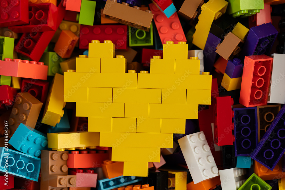 Fototapeta premium Yellow heart built from Lego bricks on colorful background of Lego pieces
