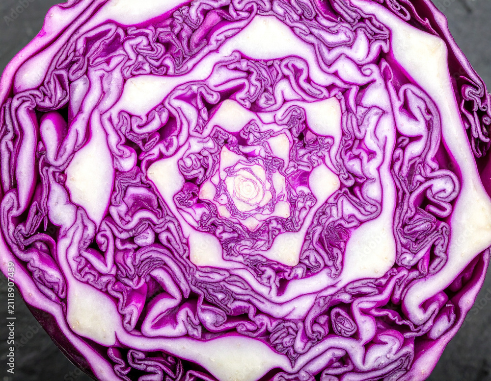 Obraz premium Macro cross section of a purple cabbage showing brain like geometric patterns on a dark stone surface.