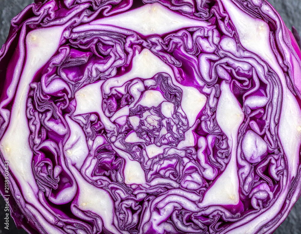 Obraz premium Macro cross section of a purple cabbage showing brain like geometric patterns on a dark stone surface.
