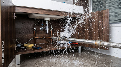 Burst Pipe Emergency: A clear instance of a burst pipe beneath a bathroom sink, causing a significant water leak and damage, highlighting a plumbing emergency.