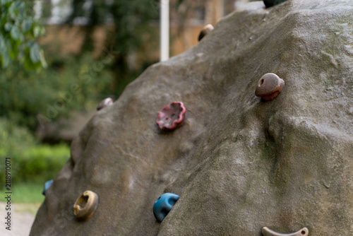 Close-up of an artificial climbing rock with colorful plastic hand and foot holds on a children's playground outdoors.