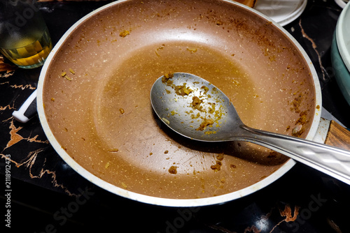 Фотография empty copper non-stick frying pan with light food residue and a large metal serving spoon resting inside