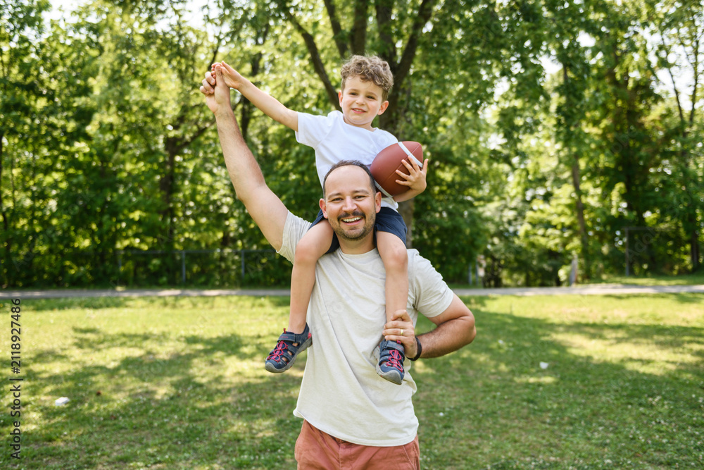 Fototapeta premium man and young boy playing american football on a court, teaching little player and spending time outdoors